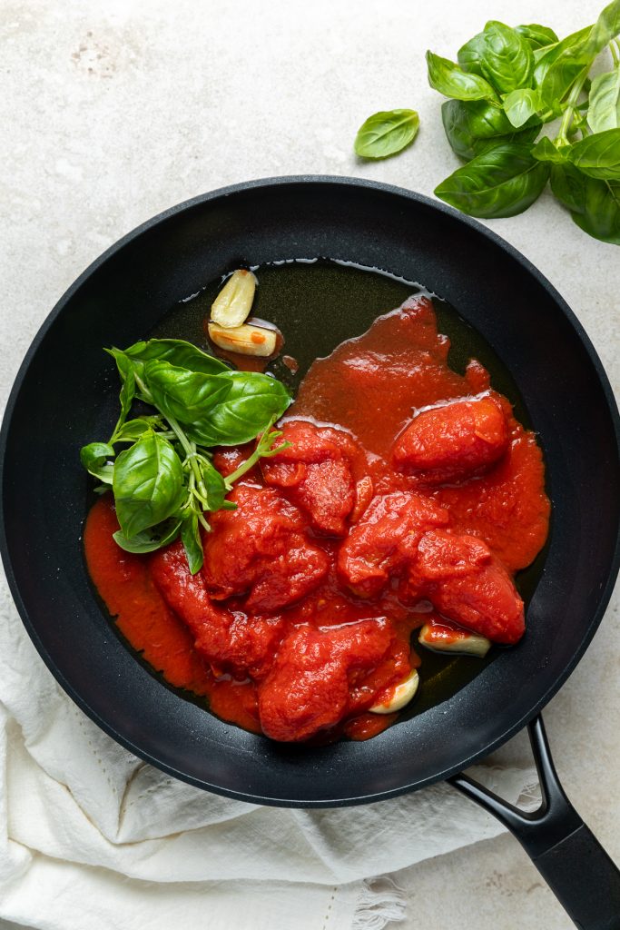 Tinned whole tomatoes and fresh basil added to the garlic in the frying pan.