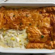 A baked chicken and leek pie with a portion taken out of the pastry to show the creamy filling.