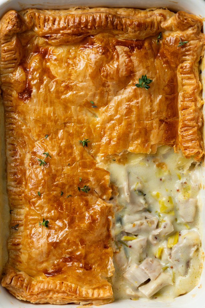 Close up of a baked chicken pie with a quarter of the pastry taken off to show the creamy chicken and leek filling underneath.