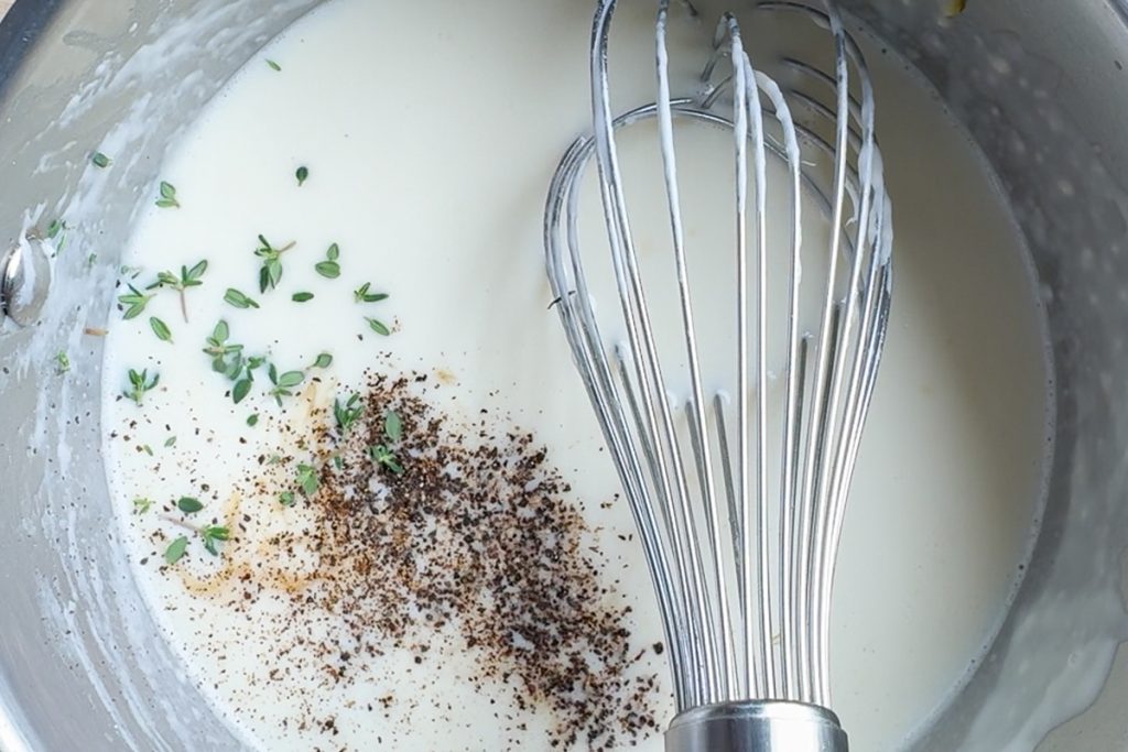 The made sauce with a balloon whisk, with fresh thyme and black pepper added to it.