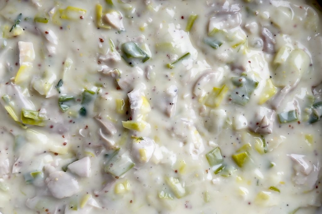 The sauce with cooked chicken and leeks added to it, poured into the baking dish.