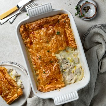 Chicken and leek pie in the baking dish, with a portion taken out and put on a plate to the left hand side of the baking dish.