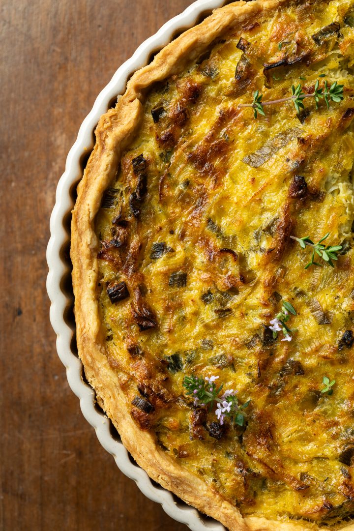 Close up of the leek tart on a wooden background, sprinkled with fresh thyme.