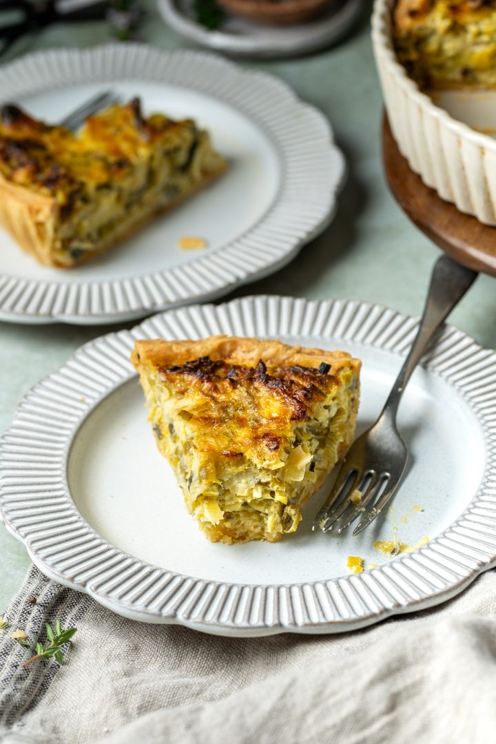 A slice of leek tart on a plate with a forkful taken off the end.