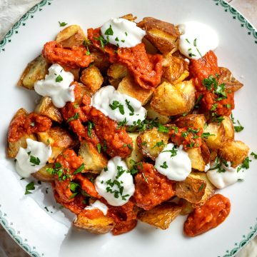 A plate of patatas bravas - crispy cubes of roast potatoes topped with spicy tomato brava sauce and roast garlic aioli.
