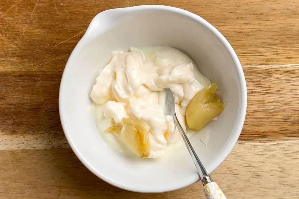 The cooked garlic added to a small bowl with mayonnaise and yogurt.