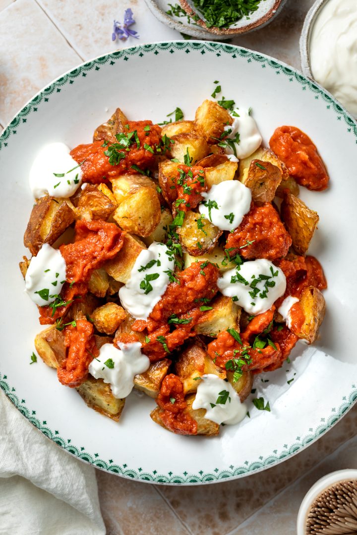 Close up of a plate of patatas bravas with garlic aioli and sprinkled with fresh parsley.