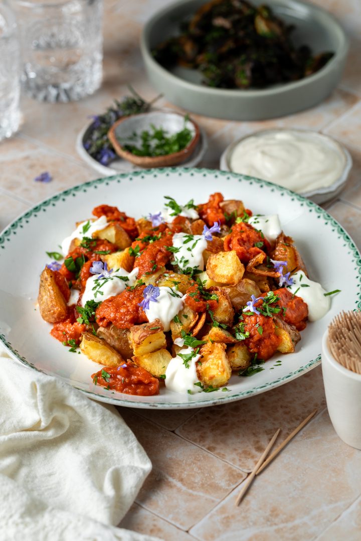 Side view of a plate of patatas bravas with a small plate of ajillo mushrooms just visible in the background.