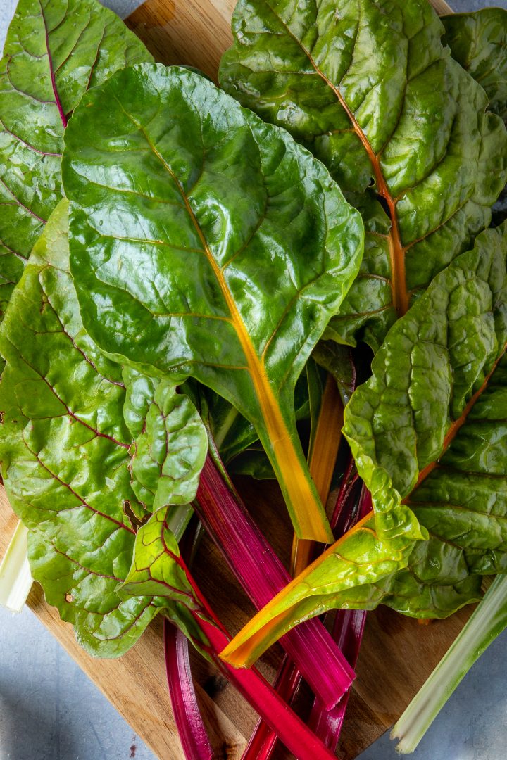 A bunch of rainbow chard on a wooden chopping board.