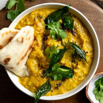 A bowl of red lentil dahl topped with curry leaves and served with a naan bread.