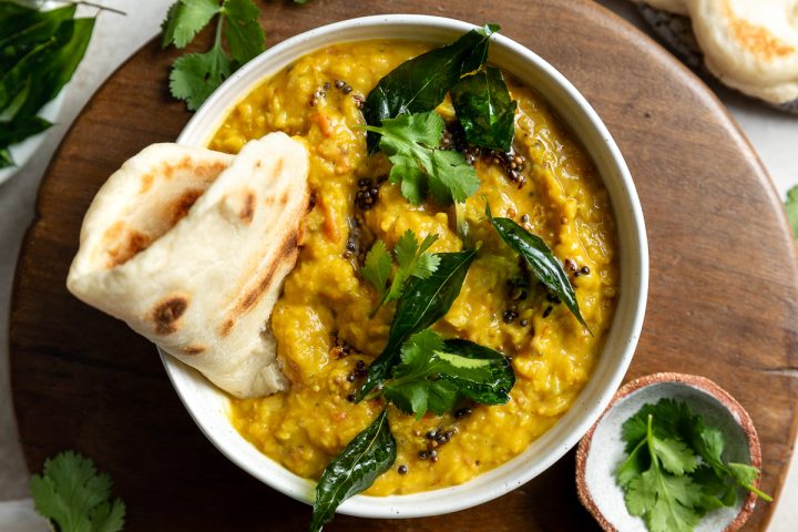 A bowl of red lentil dahl topped with curry leaves and served with a naan bread.