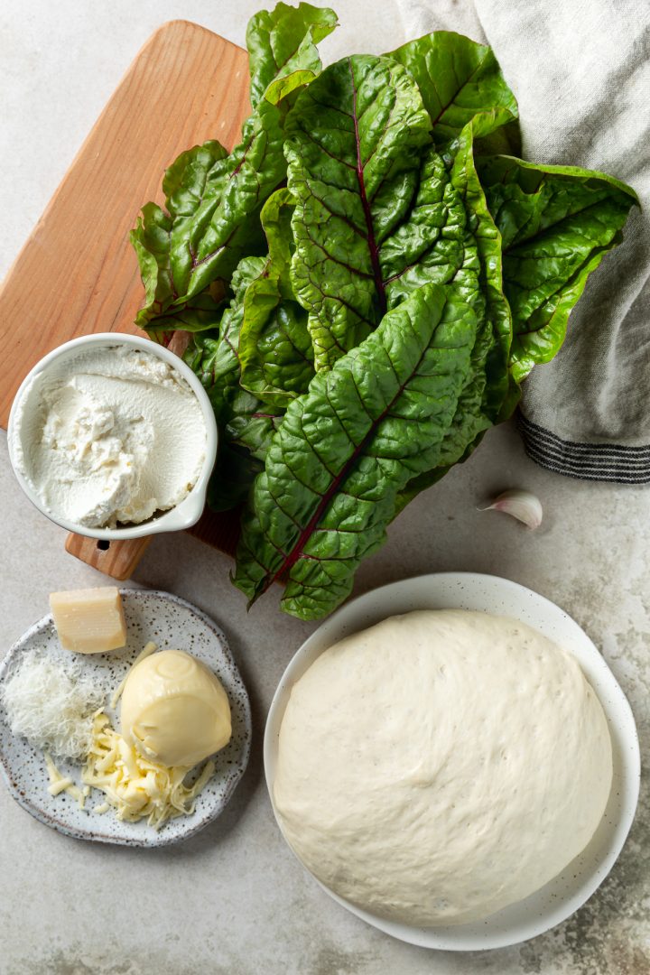 Ingredients needed to make the calzone arranged on plates and a wooden chopping board.
