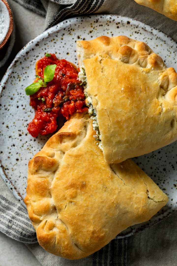 A calzone cut in half on a plate served with a fresh tomato sauce.
