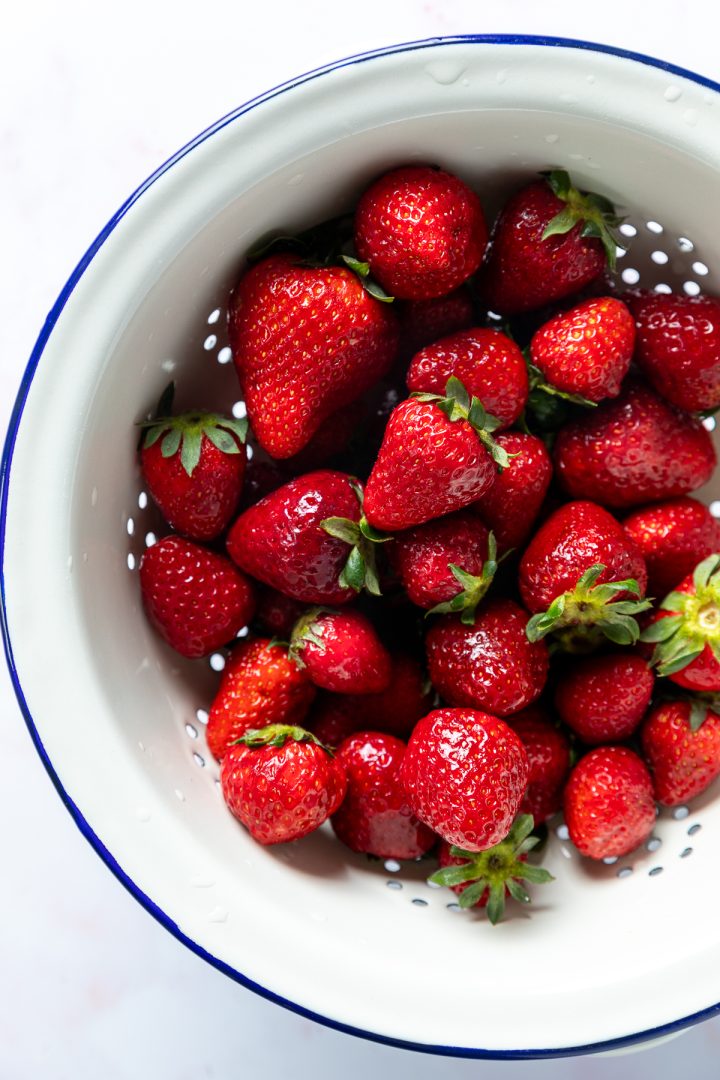 A white colander full of fresh strawberries.