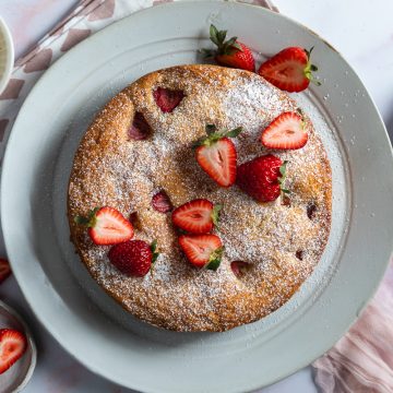 The baked strawberry cake on a serving plate topped with fresh strawberries.