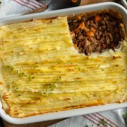 Cottage pie in a white dish with a portion of mashed potato taken off to show the beef filling below.