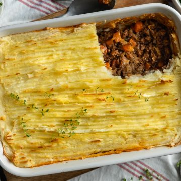 Cottage pie in a white dish with a portion of mashed potato taken off to show the beef filling below.