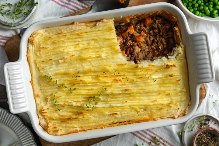 Cottage pie in a white dish with a portion of mashed potato taken off to show the beef filling below.