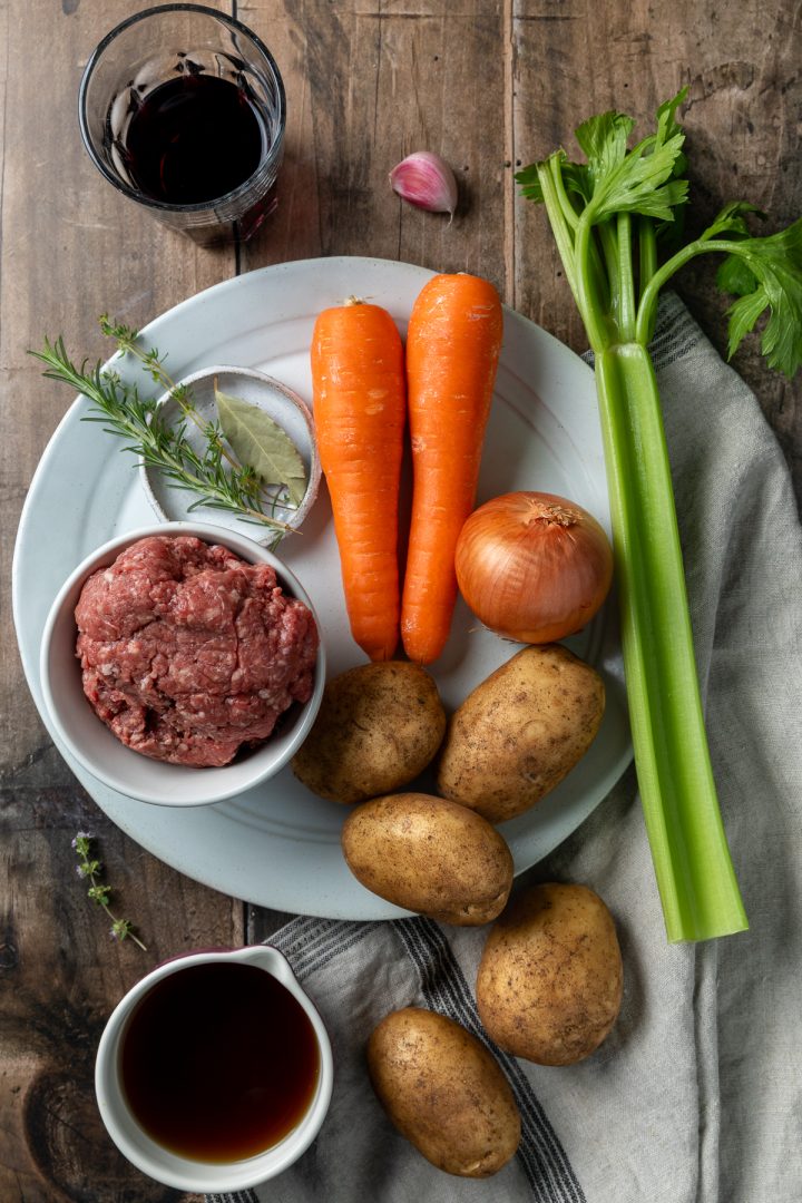 Ingredients needed to make cottage pie on wooden surface.