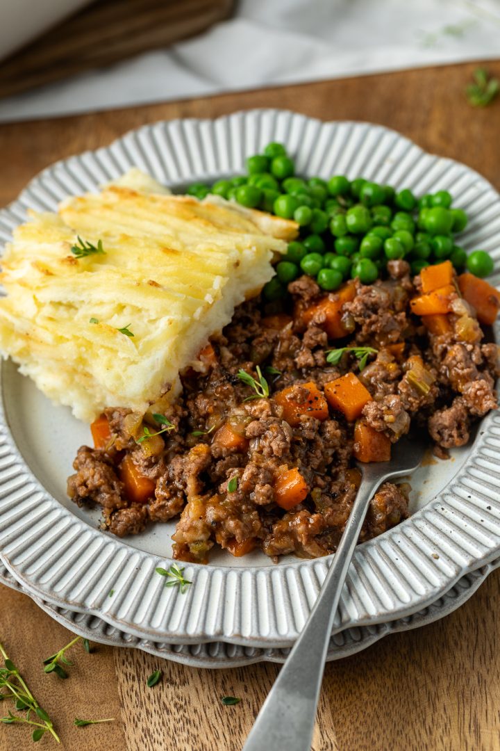 A portion of cottage pie served on a plate with peas on the side.