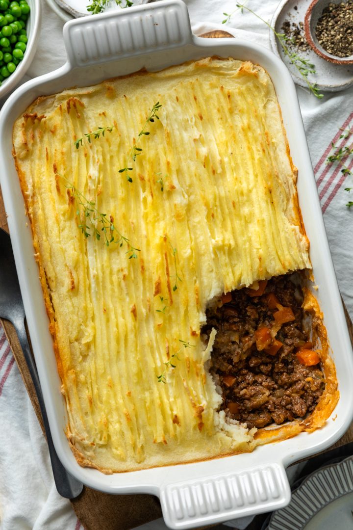 The baked cottage pie with a portion of the mashed potato topping taken out to show the juicy beef filling below.