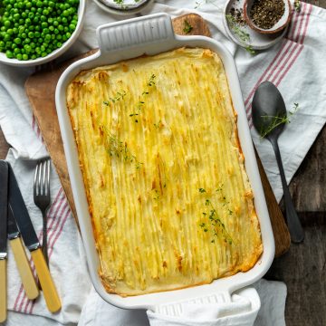 A baked cottage pie in a white dish sprinkled with fresh thyme.