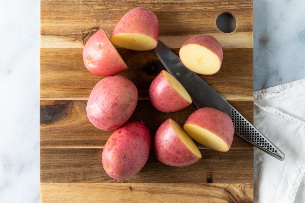 Red skinned potatoes on wooden chopping board being cut in half.