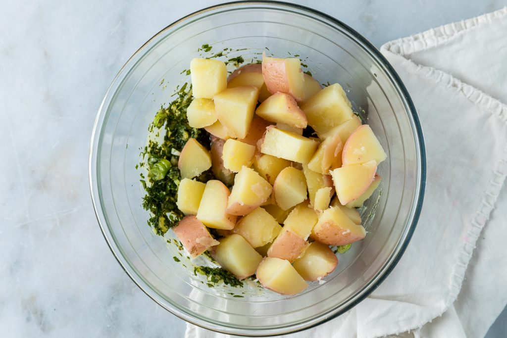 The boiled potatoes added to the bowl with the herb dressing.