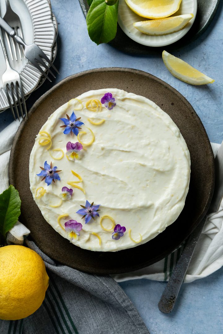 A whole lemon mascarpone cheesecake ready to serve, decorated with edible flowers.
