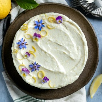 Lemon mascarpone cheesecake on a dark blue plate, decorated with lemon zest and edible flowers.