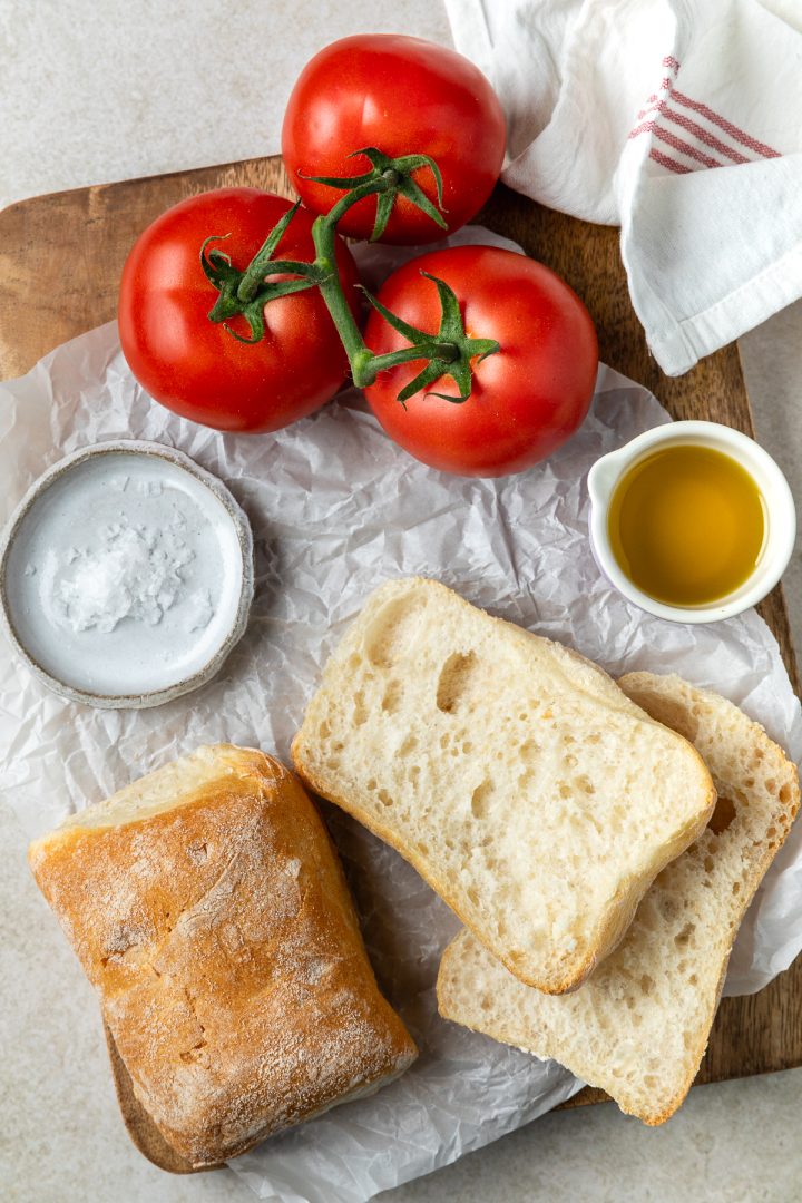 Ingredients needed to make the Spanish tomato bread on a wooden board.