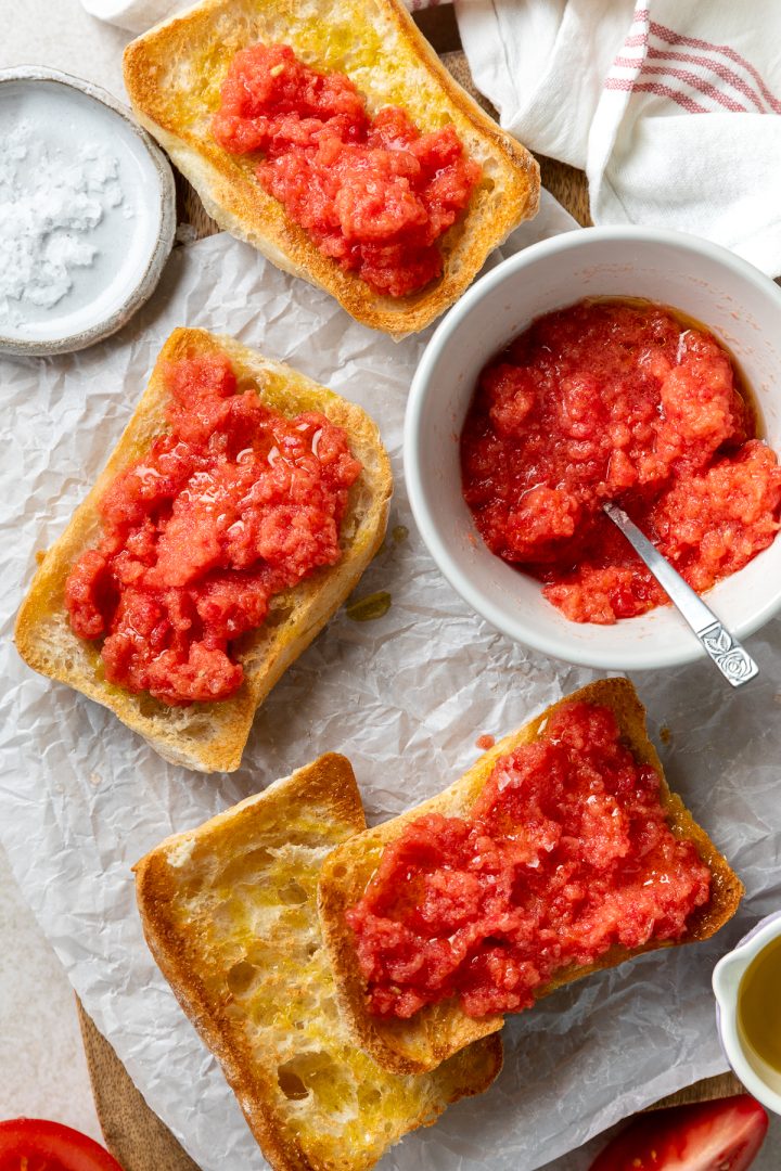 A bowl of pureed tomatoes and slices of bread drizzled with olive oil, with some of the bread slices topped with the tomato mixture.