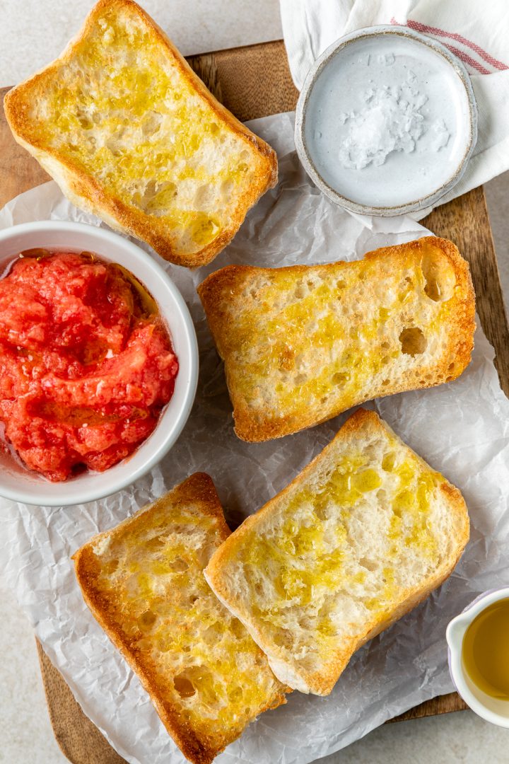 Toasted bread buns drizzled with olive oil, with a bowl of tomato puree next to them ready to serve.