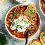 A bowl of slow cooker lasagna soup served with a slice of garlic bread.