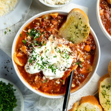 A bowl of slow cooker lasagna soup served with a slice of garlic bread.