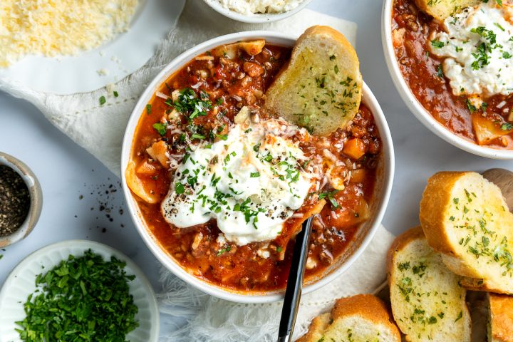 A bowl of slow cooker lasagna soup served with a slice of garlic bread.