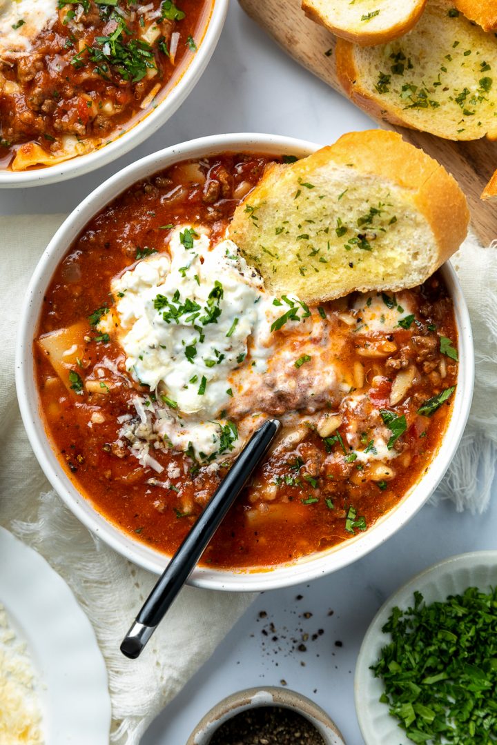 Two bowls of lasagna soup topped with ricotta, served with garlic bread.