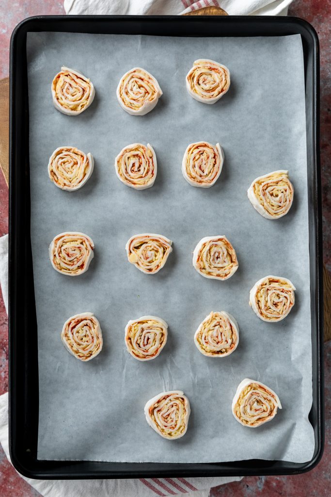 Uncooked puff pastry pinwheels on a lined tray.
