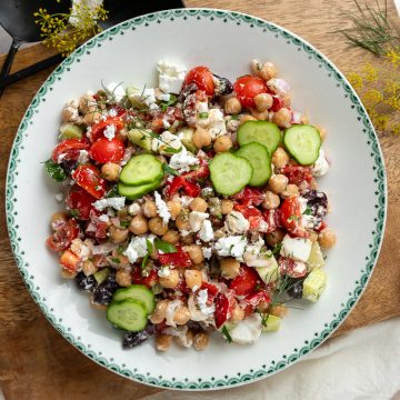 A plate of the chickpea salad on a wooden board decorated with fresh dill flowers.