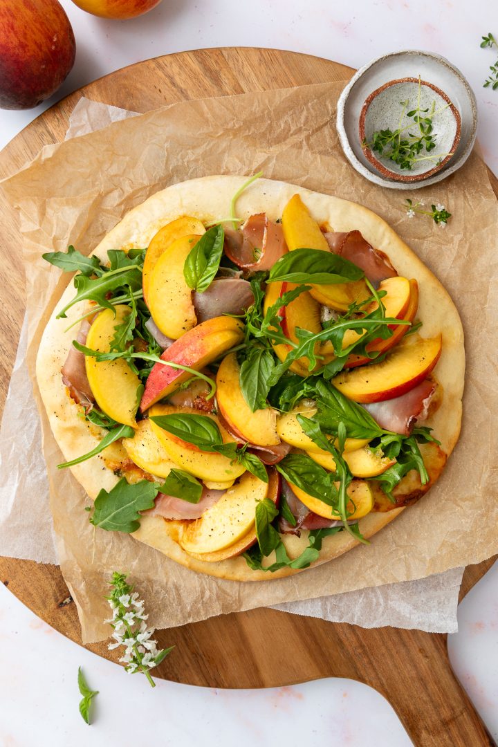The baked pizza topped with peach slices, rocket and prosciutto, with no balsamic drizzle.