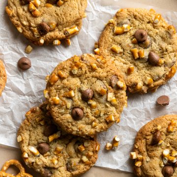 Pretzel chocolate chip cookies with chocolate chips and broken pretzels scattered around them.