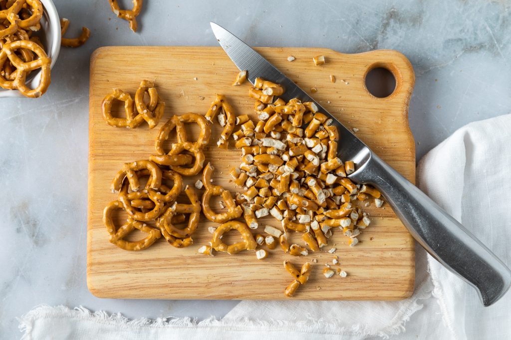 Pretzels on a wooden board being chopped with a knife.