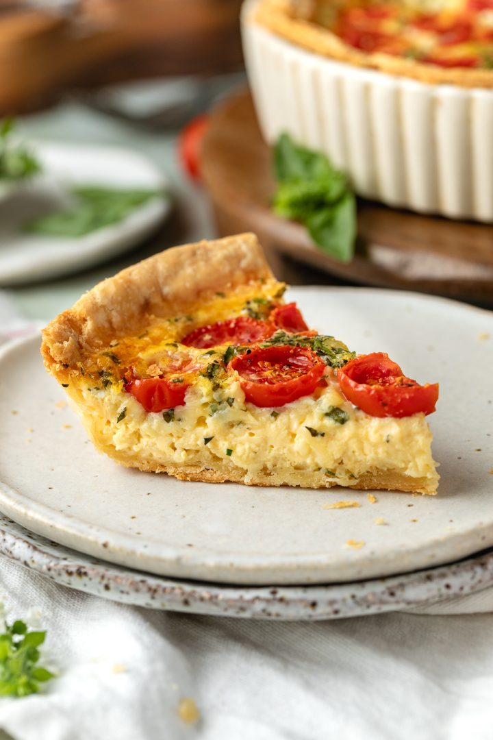 A slice of cheese and tomato quiche on a plate.