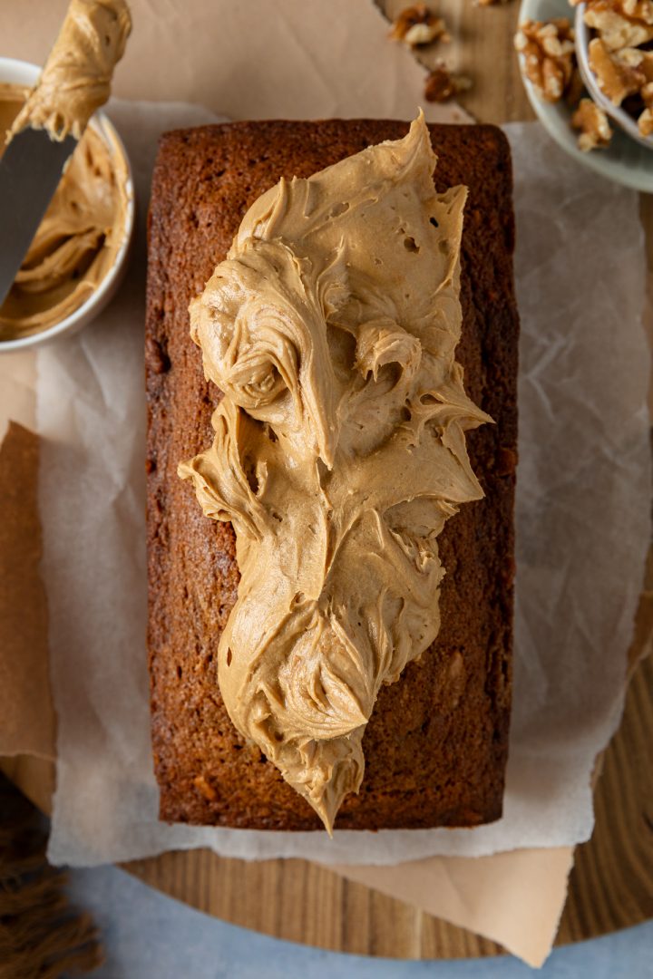 The coffee loaf cake topped with spoonfuls of coffee buttercream, yet to be spread over the top of the cake.