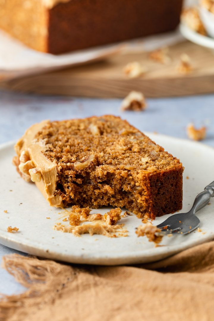 A slice of coffee walnut cake on a plate with a portion taken off one corner to show the texture of the coffee sponge.