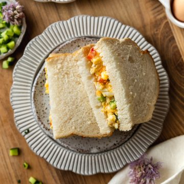 An egg sandwich cut in half on a plate, on a wooden board.