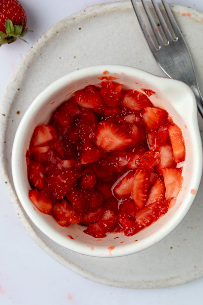 Mashed strawberries in a small bowl with a fork next to it.