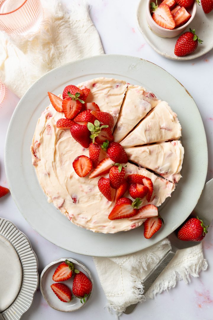 The finished strawberry cheesecake on a plate topped with fresh strawberries, with three slices cut out of it.
