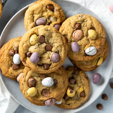 A plate of mini egg cookies, with chocolate mini eggs scattered around the plate.