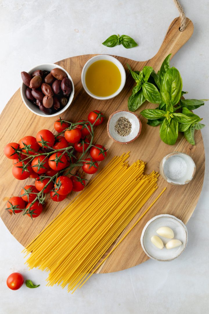 Ingredients needed to make the tomato pasta on a wooden board.